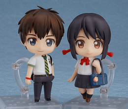 Standing male and female Chibi-style anime figurines on clear stands with a grey backdrop.